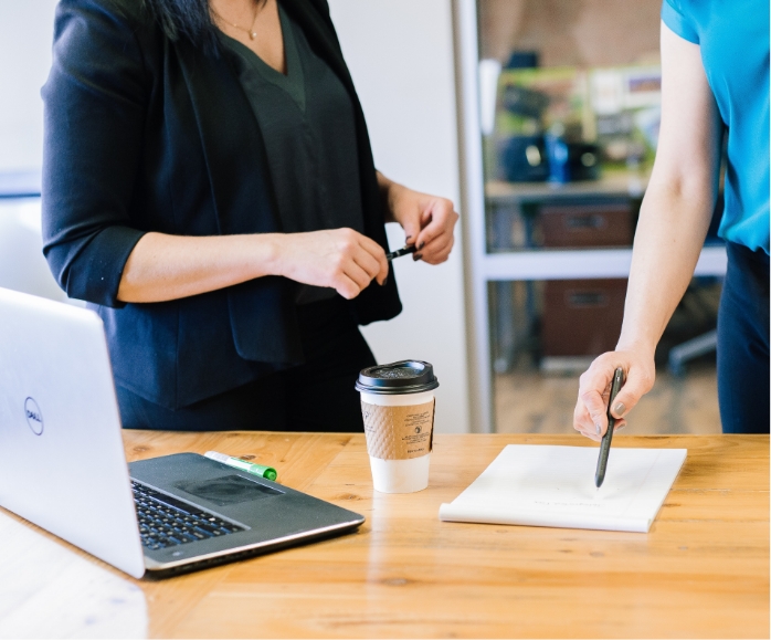 two people gathered around a table discussing. one person pointing to a piece of paper.